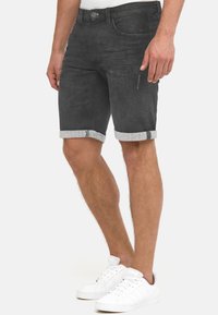 Shorts en denim noir avec une coupe ajustée, ourlets retroussés, poches avant et arrière, et détails de coutures discrètes. Associés à des baskets blanches.