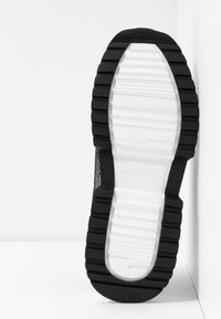 Semelle de sneaker noire et blanche avec des rainures profondes et « MICHAEL KORS » embossé au centre de la partie blanche.
