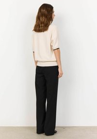 Short-sleeve, cream top with black trim paired with black, wide-leg trousers. Smooth textures, minimalistic design, and neutral colors.