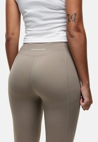 Beige legging gemaakt van rekbaar materiaal, met een hoge tailleband en zichtbare stiksels. De merknaam is op de taille gedrukt.