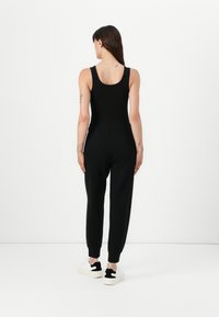 Svart tank topp parret med svarte joggesbukser, med en avsmalnende ben og ribbede mansjetter, iført hvite joggesko. Glatt tekstur, minimalistisk design.