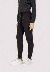 Czarne spodnie dresowe z elastycznym pasem i sznurkiem, dopasowany krój oraz wyszyte logo. Połączone z białymi sneakersami dla swobodnego wyglądu.