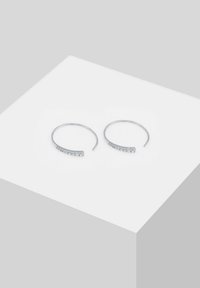 Boucles d'oreilles en argent en forme de cerceau avec un design incurvé, ornées d'une rangée de pierres transparentes sur un côté, texture lisse et dos ouvert pour un enfilage facile.