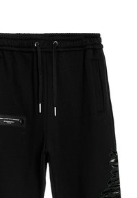 Pantalones deportivos negros con cintura elástica, cordón, bolsillos laterales y detalle de parche texturizado en la pierna. Acabado de tela suave.