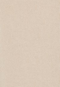 Beige ribbat textil som visar en fin, vertikal struktur med en mjuk yta, lämplig för kläder eller stoppningsapplikationer.