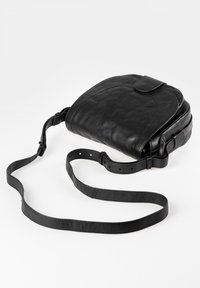 Mustan nahkainen olkalaukku, jossa on kaareva muoto, läppäsuljenta ja säädettävä hihna. Rakeinen pinta, jossa on minimaalinen varustelu.