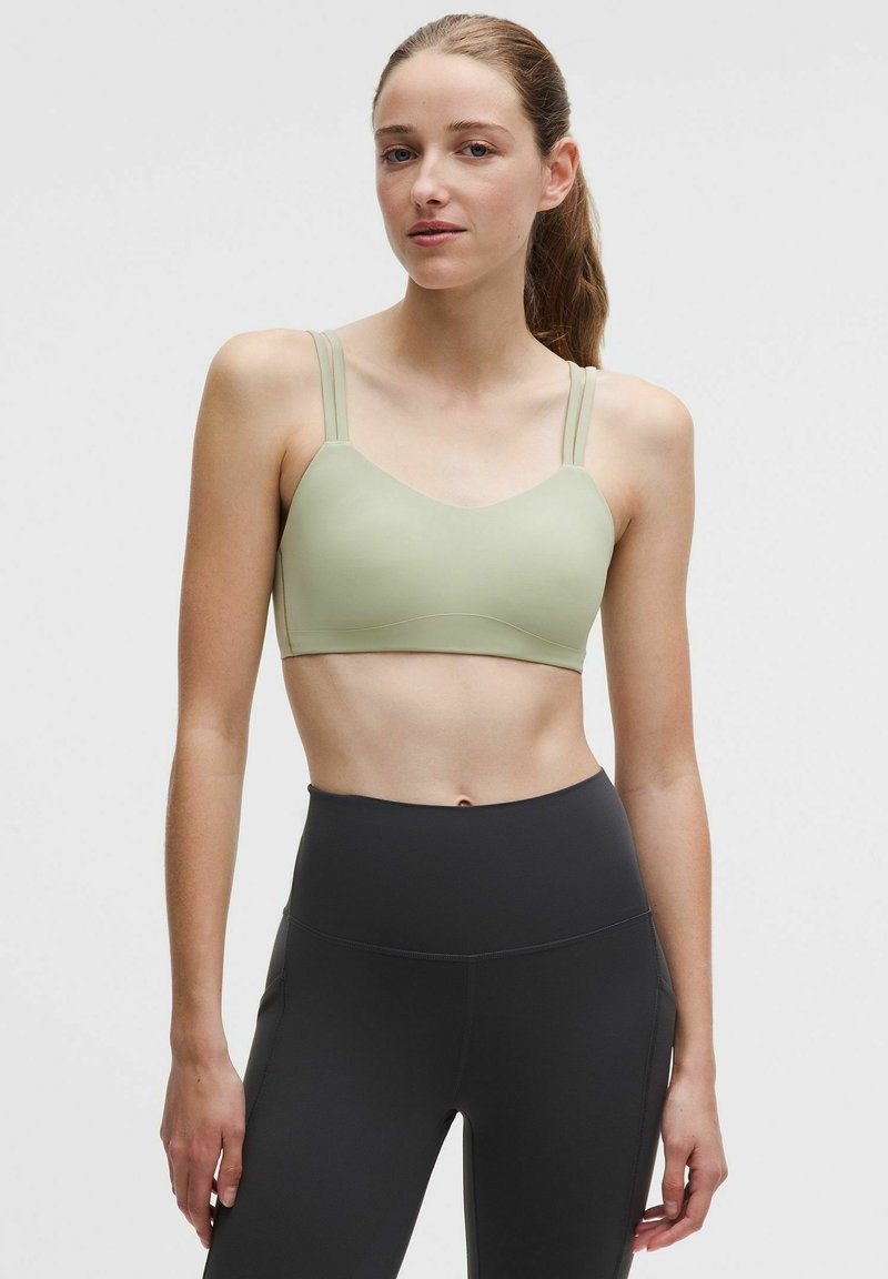 Hellgrüner Sport-BH mit verstellbaren Trägern, weicher Textur und nahtlosem Design, kombiniert mit hoch taillierten schwarzen Leggings.