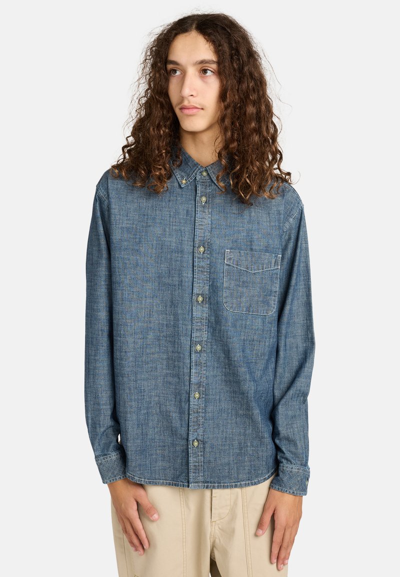 Denim overhemd met knopen in donkerblauw, met een kraag, lange mouwen en een borstzak. Het heeft een subtiel textuurpatroon en knoopsluitingen.