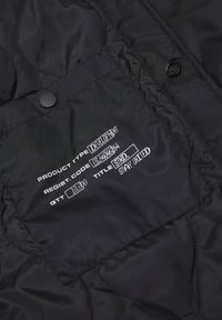 Czarna pikowana tkanina o błyszczącym wykończeniu. Zawiera metkę z białymi szczegółami na temat typu produktu, kodu rejestracyjnego i tytułu.