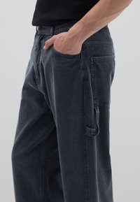 Dunkelgraue Cordhosen mit lockerem Schnitt, ausgestattet mit seitlichen und vorderen Taschen. Auffallend durch ihren strukturierten Stoff und dezente Nähte.