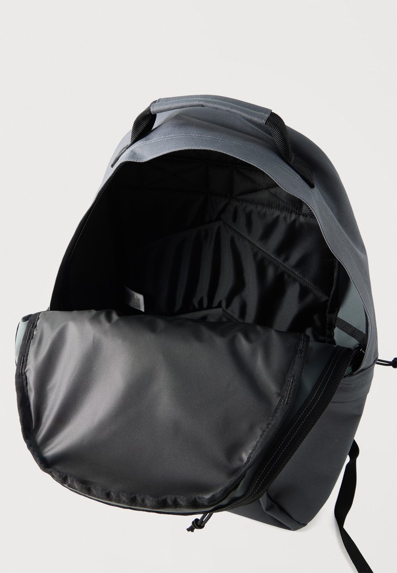 Grauer Rucksack mit vollständig geöffnetem Hauptfach, das das schwarze Innenfutter und das gepolsterte Rückenteil vor weißem Hintergrund zeigt.