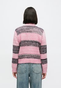 Camisola de malha com riscas horizontais cor-de-rosa, pretas e brancas, apresenta gola redonda e punhos canelados. Usada por cima de calças de ganga largas.