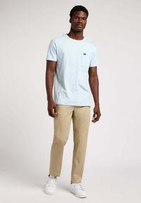 Lichtblauw T-shirt met korte mouwen en een borstzak, gecombineerd met beige broek en witte sneakers. Glad materiaal, recht gesneden silhouet.