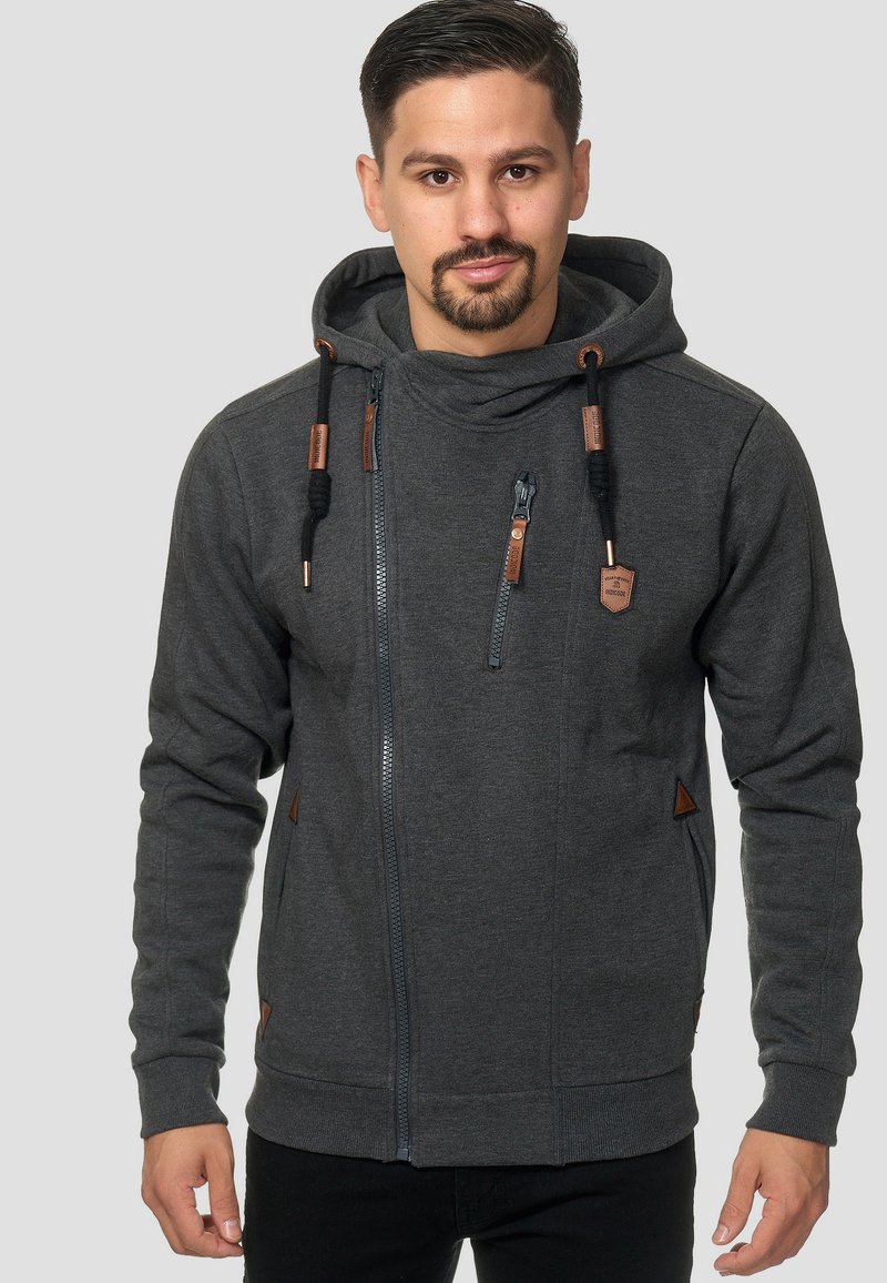 Sudadera con cremallera en gris, con un acabado texturizado, que presenta un alto cuello, cordones, bolsillos laterales y detalles de cuero en la cremallera y el dobladillo.