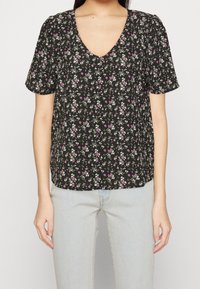 Blusa nera a fiori con scollo a V, maniche corte e vestibilità ampia. Presenta piccoli fiori bianchi e rosa su uno sfondo nero.