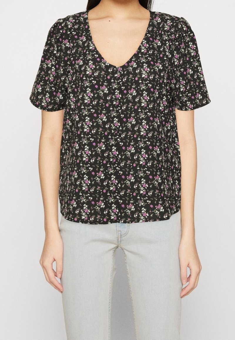 Blusa nera a fiori con scollo a V, maniche corte e vestibilità ampia. Presenta piccoli fiori bianchi e rosa su uno sfondo nero.