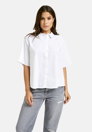 White short-sleeve button-up shirt with a collar, made of lightweight fabric, paired with distressed gray jeans.