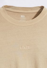 Beżowa koszulka vintage Levi's o dopasowanym kroju z okrągłym dekoltem i małym haftowanym logo Levi's na klatce piersiowej, wyprodukowana w Pakistanie.