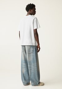 Hvid bomulds T-shirt med korte ærmer, parret med løstsiddende lyseblå denimjeans med subtil falming og store lommer.