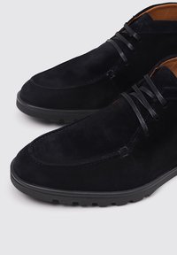 Zapatos de ante azul oscuro con una textura suave, punta redonda y suela de goma negra; presentan cordones finos y un diseño minimalista.