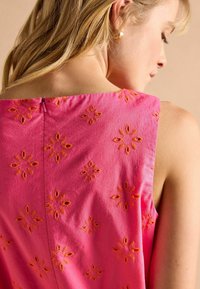 Rosa ärmelloses Kleid mit floralen Stickereien in Orange. Der Rücken hat einen sichtbaren Reißverschluss und das Material hat eine strukturierte Oberflächen mit glatter Haptik.