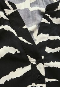Blouse noir et blanc avec un motif zèbre, dotée de boutons sur le devant et d'un décolleté en V. Tissu lisse avec des accents texturés.