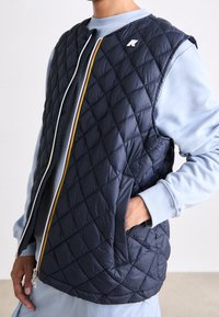 Marineblaue wattierte Weste mit hohem Kragen, Reißverschluss vorne mit mehrfarbigem Akzent und Seitentaschen. Strukturiertes Gewebe mit Rautenmuster.