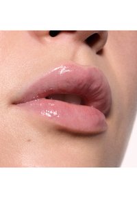 Nahaufnahme von glatten, vollen Lippen mit einem blassen Rosaton, glatter Textur und leichtem Glanz, vor neutralen Hauttönen.