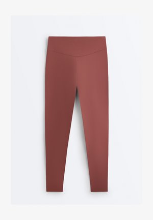 Roestbruine leggings met hoge taille en een V-vormige tailleband, plat uitgestald tegen een witte achtergrond.