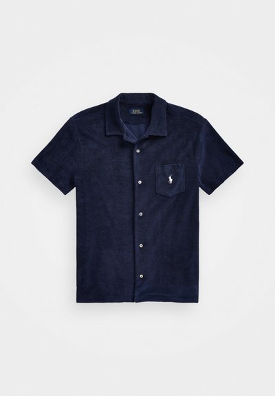 Camisa de manga corta azul marino hecha de tela texturizada, con cierre de botones en la parte delantera, cuello de punta y un bolsillo en el pecho con un logotipo.