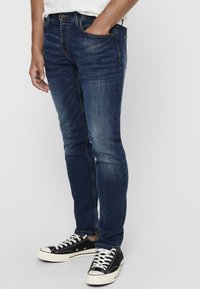 Mörkblå skinny jeans med subtila blekningar, femfickorsdesign och en klassisk knappstängning. Matchas med svarta tygskor.