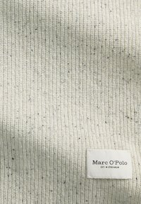 Niemal biały, dzianinowy materiał z teksturowanym, prążkowanym wzorem. Posiada małe czarne plamki i prostokątną metkę z napisem "Marc O'Polo."