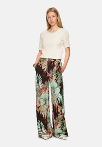 Cream short-sleeve top paired with black wide-leg pants featuring a colorful floral and leaf pattern, smooth texture, and a relaxed fit.