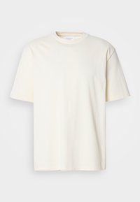 T-shirt a maniche corte e collo rotondo, di colore bianco sporco, design unisex, esposto su uno sfondo grigio neutro.