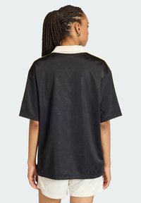 Μαύρη αθλητική φανέλα με γιακά· διαθέτει διακριτικό διαγώνιο σχέδιο, κοντά μανίκια και κίτρινες λεπτομέρειες στους ώμους.