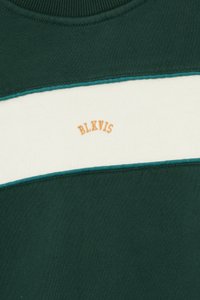 Πράσινη φόρμα με κρεμ οριζόντια ρίγα, τιρκουάζ λεπτομέρειες και κεντημένο "BLKVIS" σε πορτοκαλί στο μπροστινό μέρος. Μαλακό ύφασμα, στρογγυλή λαιμόκοψη.