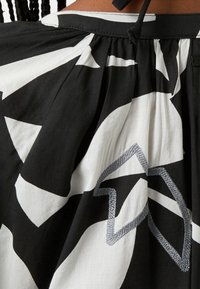 Černobílá látka se vzorovanými geometrickými designy, s plisy a stříbrně vyšitým akcentem na dolní části.