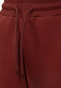 Bordeauxfarvede sweatpants med ribbet talje og snor. Stoffet er glat med en blød tekstur, og der er synlige syninger.
