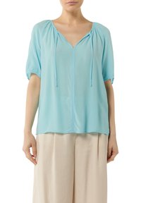 Light blue blouse made of soft fabric, featuring a v-neck, short puff sleeves, and adjustable drawstrings at the neckline.
