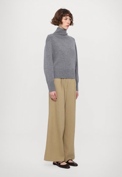 Grå turtleneck genser laget av mykt strikket stoff, sammen med vide beige bukser. Sorte flater med rund tå og aksentdetalj.