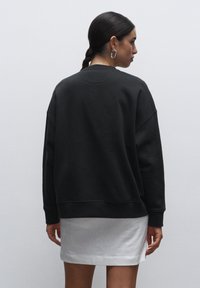 Sudadera grande de color gris oscuro con cuello redondo y mangas largas, combinada con una falda blanca. Textura suave y diseño minimalista.