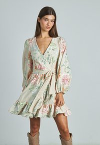 Blumen-Wickelkleid aus leichtem beigen Leinen mit mehrfarbigem Stickmuster, langen Puffärmel und einem Rüschensaum. Mit einem gebundenen Taillendetail.