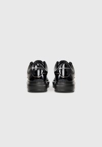 Adidași negri din piele patentată, cu spate căptușit, talpă din cauciuc și branding embosat pe călcâi. Textură netedă cu un design elegant.