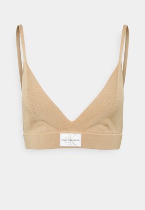 Beżowy biustonosz typu bralette o gładkiej fakturze, z trójkątnymi miseczkami i cienkimi regulowanymi ramiączkami. Na pasku pod miseczkami znajduje się naszywka z logo.