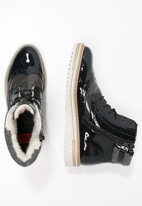 Svarta lackläder ankelskor med vit pälsfoder, sidodragkedja och beige räfflade gummisulor visade från ovan- och sidorna.