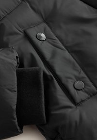 Fekete puffdzseki fényes gombokkal, puha fleece mandzsettákkal, sima, texturált anyagból, steppelt kivitelben.
