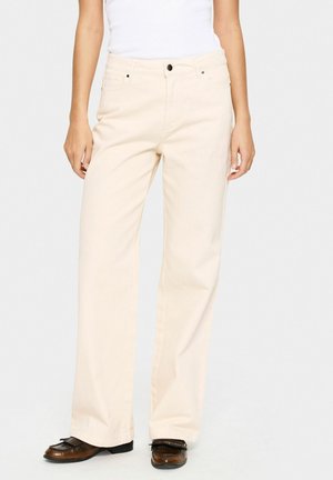 Beige wijde broek van een katoenmix stof. Heeft voorzakken, een ritssluitingen en een subtiele textuur. Gecombineerd met bruine schoenen.