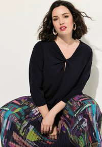 Musta toppi, jossa on V-pääntie ja solmukohta, yhdistettynä värikkääseen liehuvaan hameeseen, jossa on abstrakteja kuvioita eloisissa väreissä.