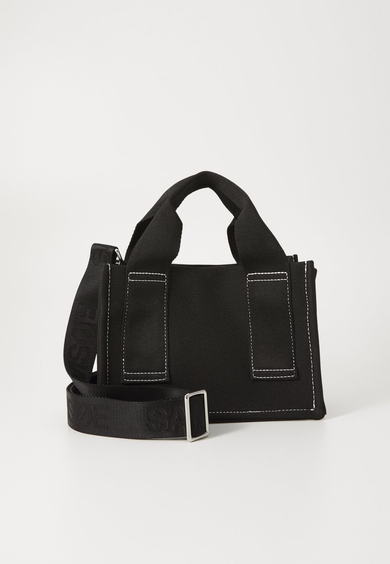 Petit sac à main en tissu noir avec doubles anses supérieures et bandoulière réglable, présentant un texte discrètement embossé.