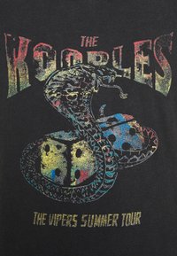 Camiseta negra con un gráfico colorido de serpiente y dados, texto "THE KOOPLES" y "THE VIPERS SUMMER TOUR" en tipografía brillante y en negrita.